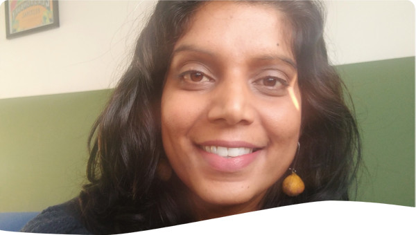 Female, indian origin, wearing blue jumper, yellow earrings, hair down